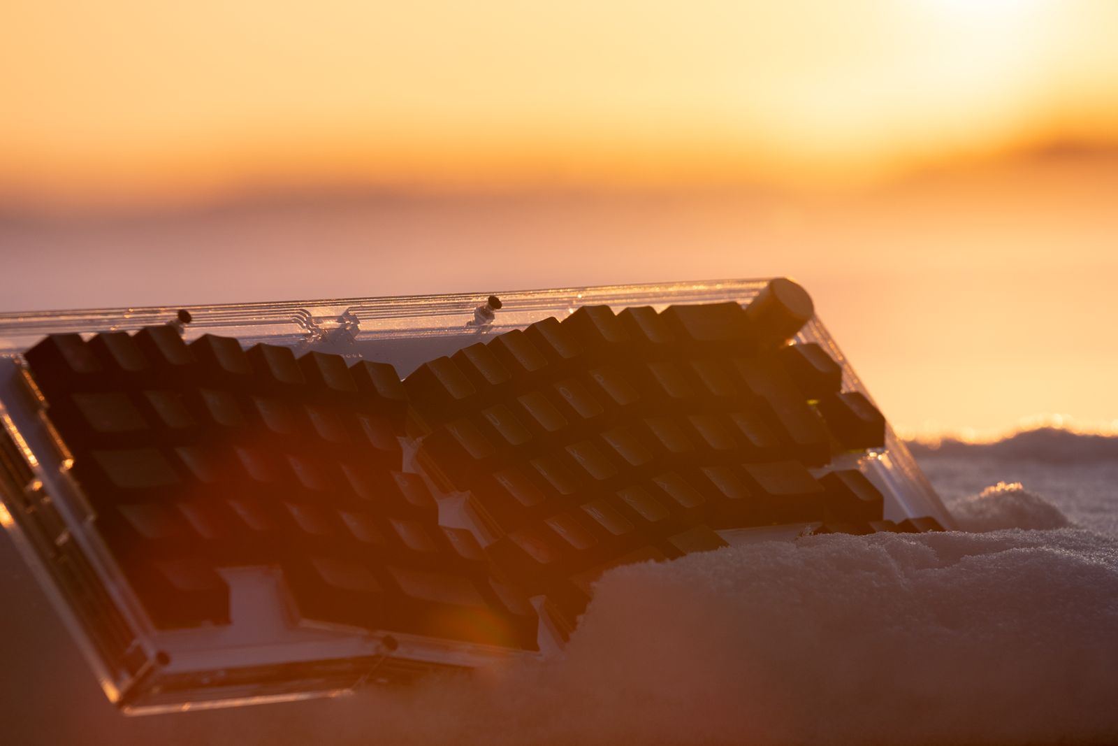 A keyboard sitting in the snow at sunrise